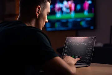 A man celebrating a winning moment on his laptop while gaming symbols float around him, capturing the excitement of BK66 games.